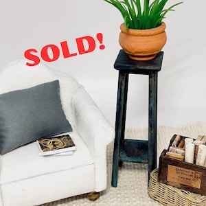 May include: Miniature scene with a white armchair, gray pillow, and a small table holding a terracotta pot with green plants. A wooden crate and basket are also present. The text "SOLD!" and "Do Not buy - Sample Work!" are visible.