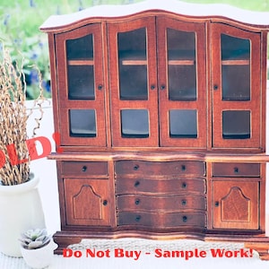May include: A miniature wooden hutch with glass-paned doors and drawers. The hutch is a rich brown color and has a curved top. The word "SOLD!" is written across the image in red. The text "Do Not Buy - Sample Work!" is also visible.