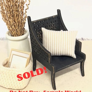 May include: Miniature black wooden chair with a striped pillow. A white woven basket holds two small framed pictures. A white vase with dried decorative stems is also present. The word "SOLD!" is written in red.