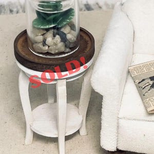 May include: Miniature white side table with a round top and a lower shelf. A small glass jar with a green plant and pebbles sits on the table. The word "SOLD!" is stamped across the top. The text "Do Not Buy - Sample Work!" is at the bottom.