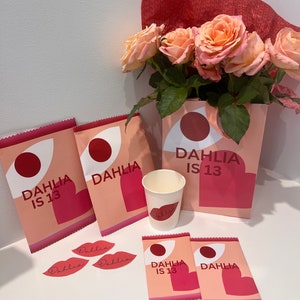 以下が含まれることがあります： 花をテーマにしたパーティー用品のコレクション。 ピーチ色のバラの花束、ギフトバッグ、ステッカー、紙コップが含まれています。 バッグとカップには、スタイリッシュなフォントで「DAHLIA IS 13」と「Dahlia」の文字と、唇のグラフィックが描かれています。