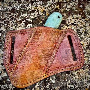 May include: A brown leather knife sheath with a decorative pattern and a light blue knife blade sticking out of the top.