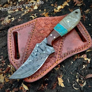 May include: A Damascus steel knife with a brown wood handle and a white and turquoise handle. The knife is in a brown leather sheath with decorative stitching.
