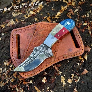 May include: A small, curved knife with a textured blade and a red, white, and blue handle with a star. The knife is in a brown leather sheath with decorative stitching.