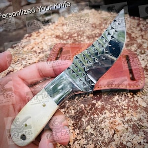 May include: A small, silver knife with a white handle and a textured blade. The knife is being held in a hand and is resting on a brown surface.