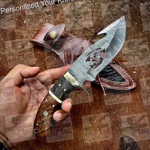 May include: A handmade knife with a Damascus steel blade and a wooden handle. The blade has a unique design with a cutout of a scorpion. The knife is shown with a leather sheath.
