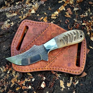 May include: A small, handmade knife with a brown leather sheath. The knife has a bone handle with a textured pattern and a serrated blade. The sheath has a decorative pattern and the words "Viper Edge" are embossed on it.
