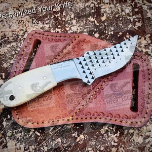May include: A small, stainless steel knife with a bone handle and a textured blade. The knife is in a brown leather sheath with the words "VIPER EDGE USA HANDMADE KNIVES" embossed on it.