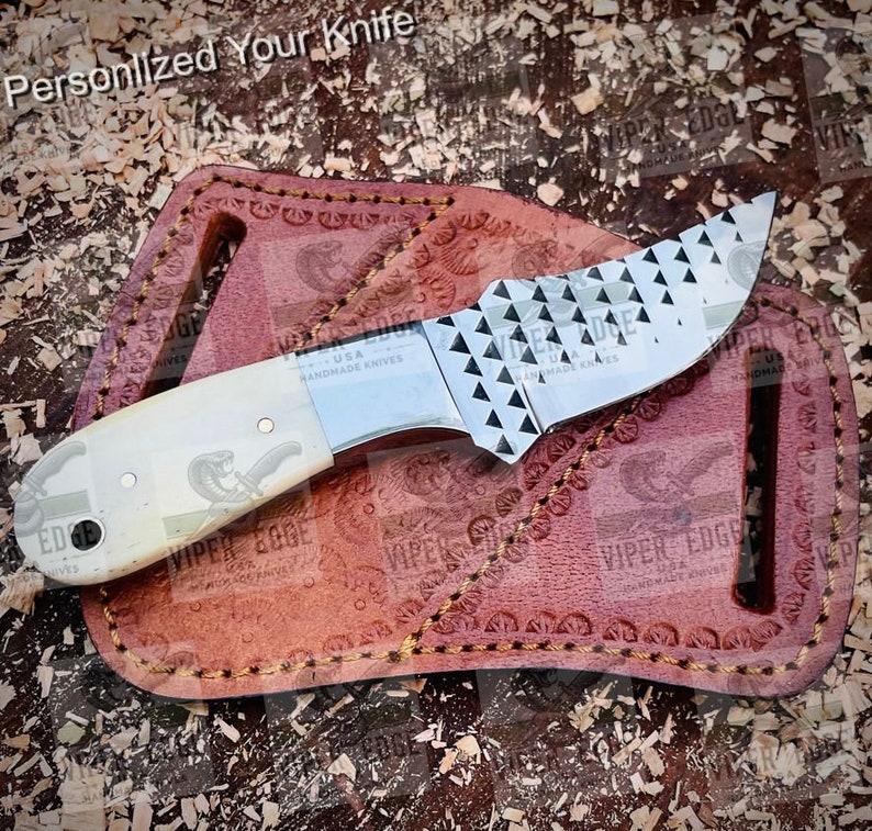 May include: A small, stainless steel knife with a bone handle and a textured blade. The knife is in a brown leather sheath with the words "VIPER EDGE USA HANDMADE KNIVES" embossed on it.
