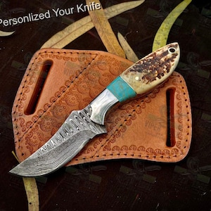 May include: A personalized knife with a damascus steel blade and a bone handle with turquoise accents. The knife is in a leather sheath with decorative stitching.