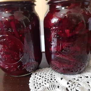 Peut inclure: Deux bocaux en verre remplis d'une relish de betteraves rouge foncé. Les bocaux ont une surface texturée et sont remplis de relish, visible à travers le verre.