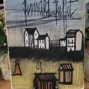 May include: A black and white print of a village scene by Bernard Buffet. The print features a series of houses with black outlines and white interiors. The sky is a light blue with grey clouds. The print is signed in the top right corner.