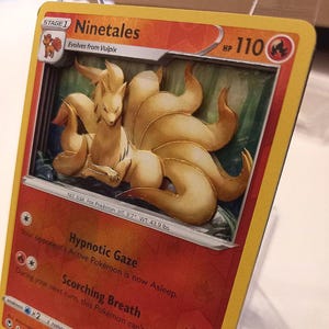 Puede incluir: Una carta Pokémon de Ninetales con un diseño esculpido en 3D. La carta presenta una criatura parecida a un zorro con nueve colas, sobre un fondo de bosque. El texto de la carta incluye el nombre "Ninetales", HP 110 y otros detalles del juego. El zorro mide 1,09 metros y pesa 19,9 kg.