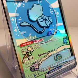 Può includere: Una carta collezionabile Pokémon Mew ex olografica. La carta presenta un personaggio Mew azzurro su uno sfondo di cielo blu. La carta ha il testo "Mew ex", "Restart" e "Genome Hacking".