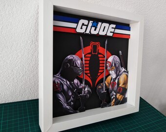 Puede incluir: Obra de arte enmarcada con dos personajes de G.I. Joe con espadas, sobre un fondo negro con el logo de Cobra. El logo de G.I. Joe se muestra en la parte superior. La obra está en un marco blanco.