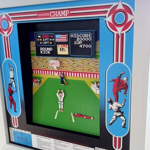 May include: A framed artwork featuring a retro video game scene. The game, "Karate Champ," is displayed with pixelated characters in a fighting arena. The frame has a blue and red design with the game's title at the top and game instructions at the bottom.