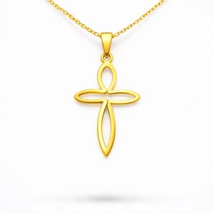 May include: A gold-colored pendant necklace featuring a stylized cross design. The cross has an open, flowing shape with rounded edges. The necklace chain is also gold and delicate, hanging against a white background.