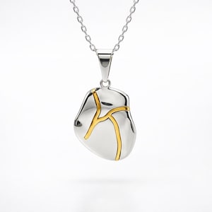 May include: A silver-tone pendant necklace with a unique design. The pendant is a smooth, irregular shape with gold-colored lines. The necklace chain is also silver-toned, creating a minimalist and elegant look.