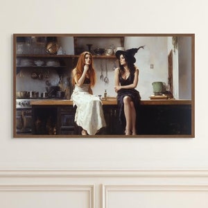Op de afbeelding: Een ingelijst kunstwerk toont twee vrouwen die op een aanrecht in de keuken zitten. De ene draagt een witte jurk, de andere een zwarte jurk en een heksenhoed. De keuken heeft donkere houten kasten, planken met keukengerei en een fornuis. Het kunstwerk hangt aan een witte muur met decoratieve lijstwerk.