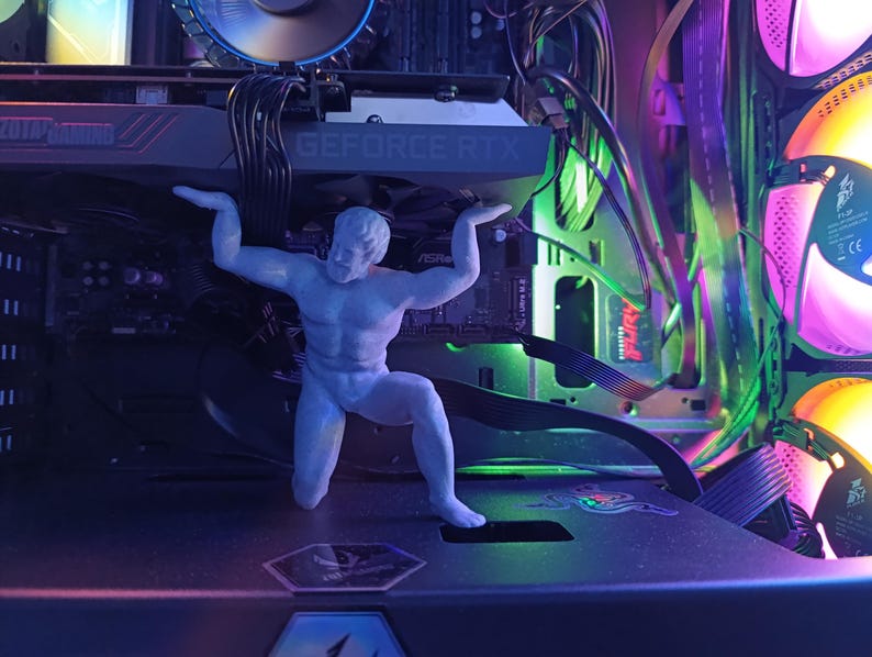 K&ouml;nnte beinhalten: Eine wei&szlig;e Plastikfigur eines Mannes in heroischer Pose, die ein Gewicht hochh&auml;lt. Die Figur steht vor einem Computergeh&auml;use mit bunten Lichtern und einer Grafikkarte mit der Aufschrift "GEFORCE RTX".