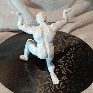 K&ouml;nnte beinhalten: Eine wei&szlig;e, 3D-gedruckte Figur eines Menschen in einer hockenden Pose mit erhobenen Armen &uuml;ber dem Kopf.