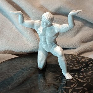 K&ouml;nnte beinhalten: Eine wei&szlig;e, 3D-gedruckte Figur eines Menschen in einer knienden Pose mit erhobenen Armen. Die Figur steht auf einer schwarzen, gemusterten Oberfl&auml;che.