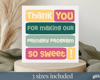 May include: A white card with colorful text that reads "Thank You For Making Our Primary Program So Sweet!" The text is in yellow, pink, teal, and green. The card is on a wooden stand.