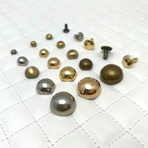 Puede incluir: Surtido de tachuelas redondas de metal en varios tamaños y acabados, incluyendo oro, plata y latón. Las tachuelas tienen una forma abovedada y son ideales para agregar un toque decorativo a artículos de cuero, ropa y otras artesanías.