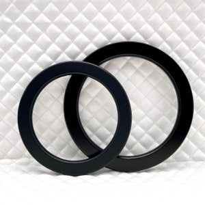 Peut inclure: Deux cadres circulaires noirs de tailles différentes, l'un à l'intérieur de l'autre, sur un fond blanc matelassé.