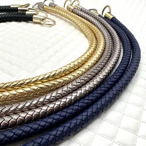 Puede incluir: Cinco cordones de cuero trenzados en azul marino, plata y oro. Los cordones están dispuestos en semicírculo y tienen cierres metálicos en los extremos.