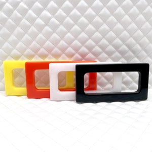 Op de afbeelding: Vier rechthoekige plastic frames in geel, oranje, wit en zwart. De frames zijn in een rij van links naar rechts gerangschikt, met de gele frame aan de linkerkant en de zwarte frame aan de rechterkant.