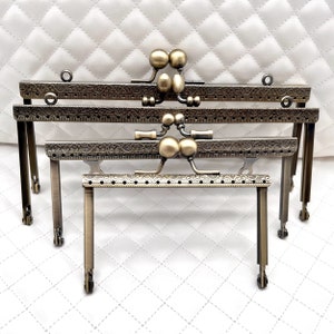 May include: Three antique gold-toned metal purse frames with ornate designs and decorative ball-shaped clasps. The frames are arranged in descending size order.
