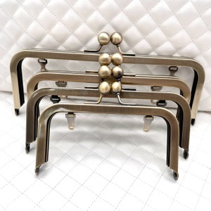 May include: Four antique brass purse frames with a decorative ball clasp. The frames are stacked on top of each other.