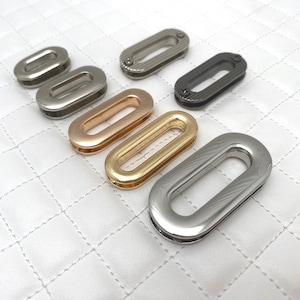 May include: Assortment of oval metal rings in various finishes, including silver, gold, rose gold, and black. The rings have a textured surface and a smooth, oval opening.