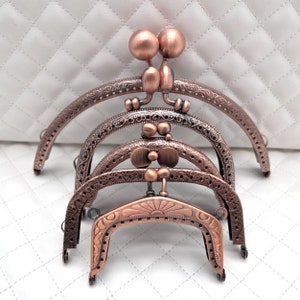 Może przedstawiać: Cztery antyczne, miedziane ramki do torebki z ozdobnymi wzorami. Ramki są ułożone jedna na drugiej, przy czym największa ramka znajduje się na dole, a najmniejsza na górze.