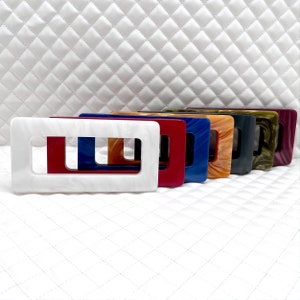 Könnte beinhalten: Ein Satz von acht rechteckigen Plastiktütengriffen in verschiedenen Farben, darunter Weiß, Rot, Blau, Orange, Braun, Schwarz, Grün und Braun mit weißen Wirbeln. Die Griffe haben einen rechteckigen Ausschnitt in der Mitte.