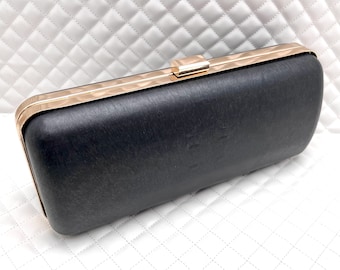 Può includere: Una pochette nera con cornice e chiusura in metallo dorato. La pochette ha una forma leggermente curva e una finitura spazzolata.