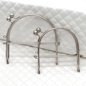 Könnte beinhalten: Zwei silberne Metall-Handtaschenrahmen mit abgerundeten Oberseiten und einer geraden Stange am Boden. Die Rahmen sind ineinander verschachtelt, wobei der größere Rahmen oben liegt.