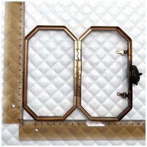 Pu&ograve; includere: Una cornice in metallo dorato per una pochette. La cornice &egrave; ottagonale e ha una chiusura a cerniera. La cornice &egrave; mostrata su uno sfondo di tessuto trapuntato bianco. La cornice &egrave; lunga 40,6 cm e larga 12,7 cm.