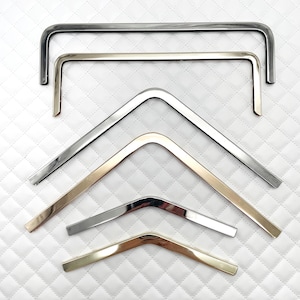 May include: Six metal bag handles in different sizes and finishes. The handles are made of silver and gold metal. The handles are arranged in a staggered pattern.