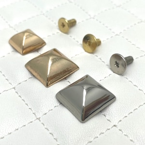 Peut inclure: Trois clous en métal en forme de pyramide avec des vis. Deux clous sont dorés et un est argenté.