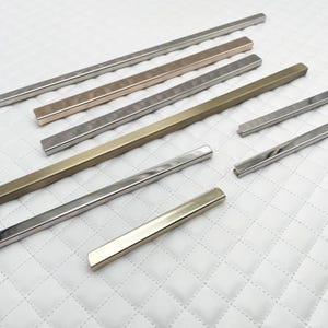 Può includere: Assortimento di pezzi di rivestimento in metallo in diverse finiture, tra cui argento, oro e oro rosa. I pezzi di rivestimento sono di forma rettangolare e hanno una superficie liscia e lucida.