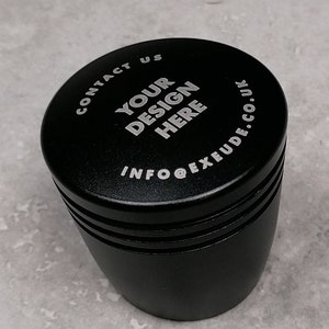 Puede incluir: Tapón de botella de metal negro con el texto "CONTACT US YOUR DESIGN HERE INFO@EXUDE.CO.UK" grabado en la parte superior.