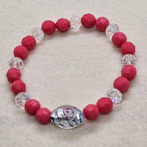 Puede incluir: Un brazalete de cuentas rosas y transparentes con una cuenta de vidrio plateada y azul en el centro.