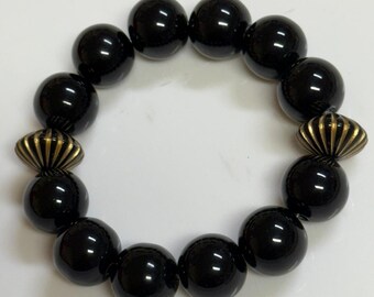 May include: A black onyx beaded bracelet with gold accents. The bracelet has a total of 12 beads, each with a smooth, polished finish. The gold accents are small, decorative pieces that add a touch of elegance to the bracelet.