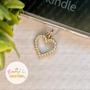 May include: A gold heart charm with clear rhinestones. The charm is on a white background with the text "Emmy L. Creations" in a circle.