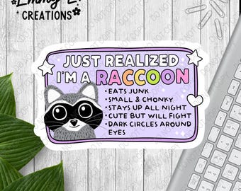 May include: A purple sticker with a cartoon raccoon and the text "Just realized I'm a raccoon" with a list of characteristics: "Eats junk", "Small & chonky", "Stays up all night", "Cute but will fight", "Dark circles around eyes".