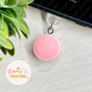 May include: A pink and white macaron charm with a silver loop for attaching to a phone case or bag.