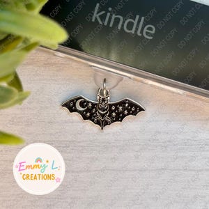 May include: A silver bat bookmark with a black enamel finish. The bat has a crescent moon and stars on its wings. The bookmark is attached to a silver chain.