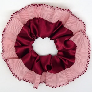 Peut inclure: Un chouchou avec une couche extérieure plissée rose clair et une couche intérieure en satin bordeaux foncé. Les bords sont finis avec une couture bordeaux foncé. Cet accessoire pour cheveux est conçu pour maintenir les cheveux en place.